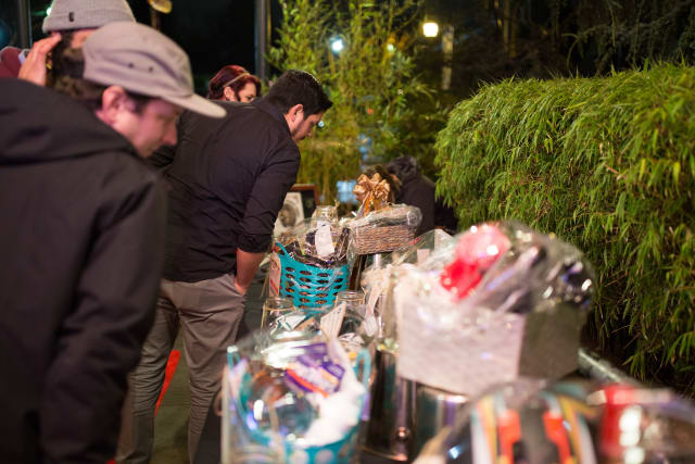 Guests examining silent auction items at the Love Bomb 2017 event, featuring baskets and gifts in a festive outdoor setting.